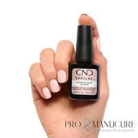 Main présentant une manucure nude beige rosé clair avec le flacon CND Shellac Naked Naivete 12,5 ml